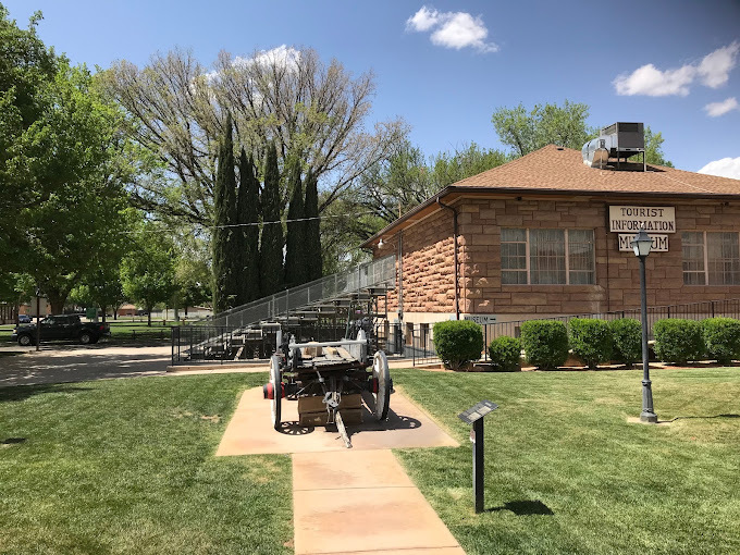 A view outside of a brown building with an old wagon out front surrounded by a grassy area.
