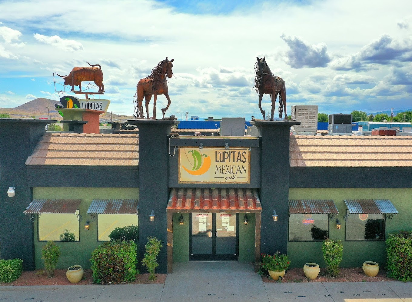 An outside view of a restaurant with two large horses out front on the roof of the building.