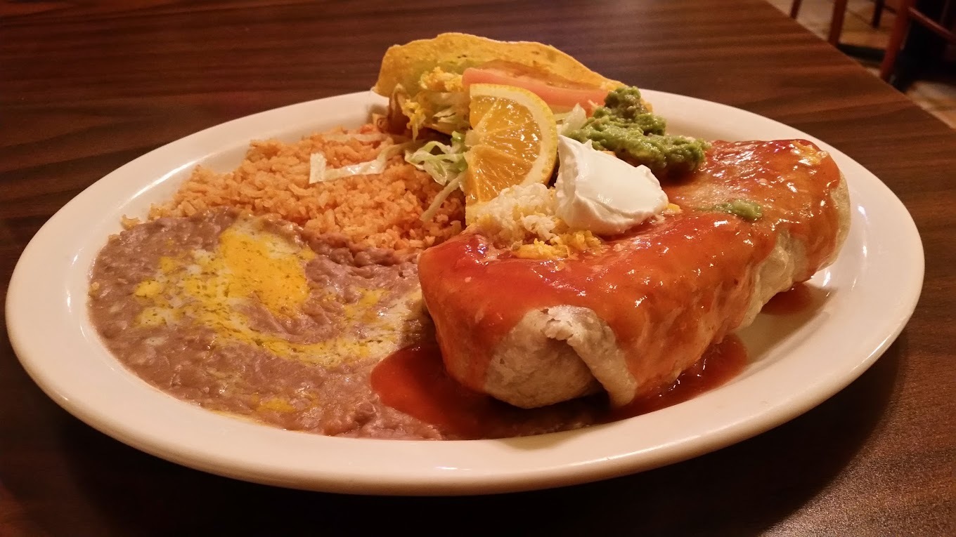 A white plate with rice and beans, an enchilada and a side of guacamole, lettuce and sour cream.