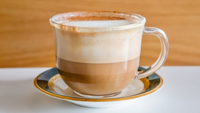 A white plate with blue and gold edging consisting of a clear glass cup with a coffee.