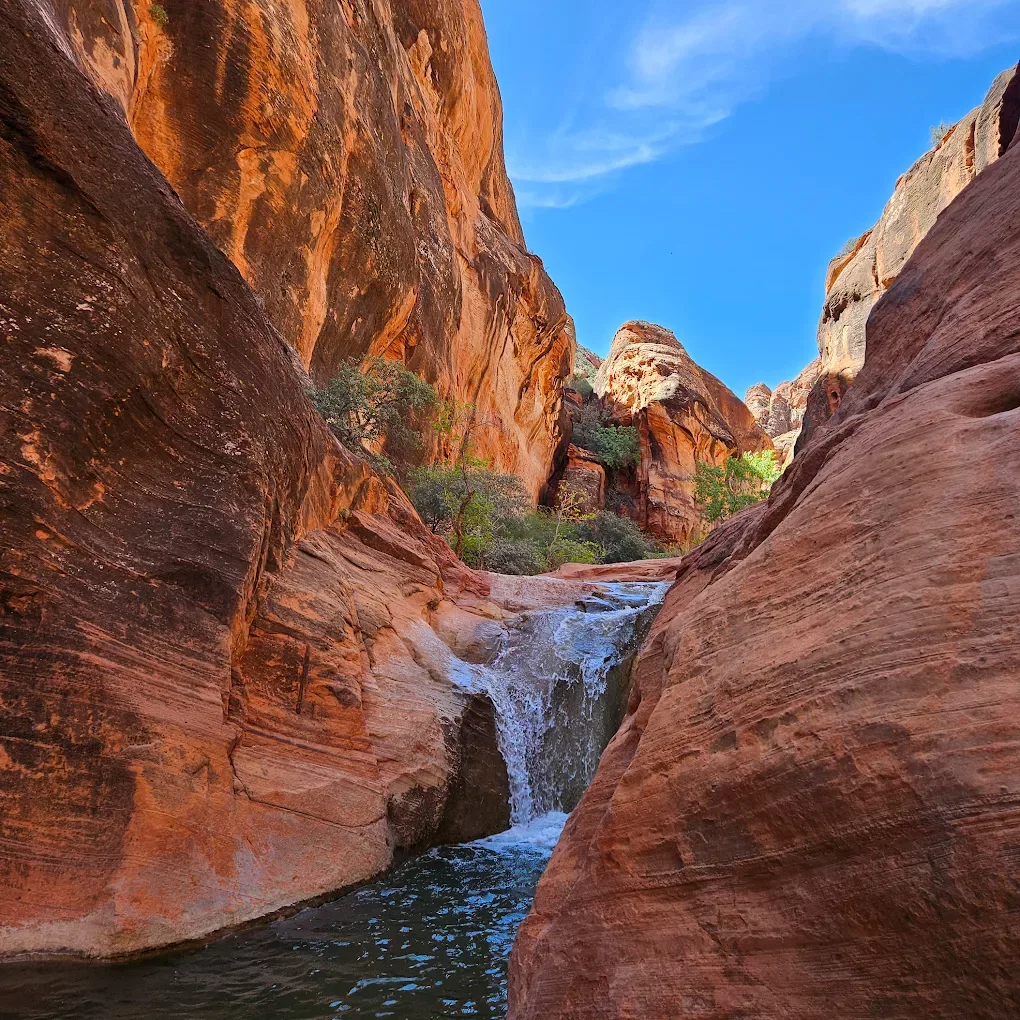 A view of two large red rock formations with a river flowing through the middle- and a waterfall trickling down.