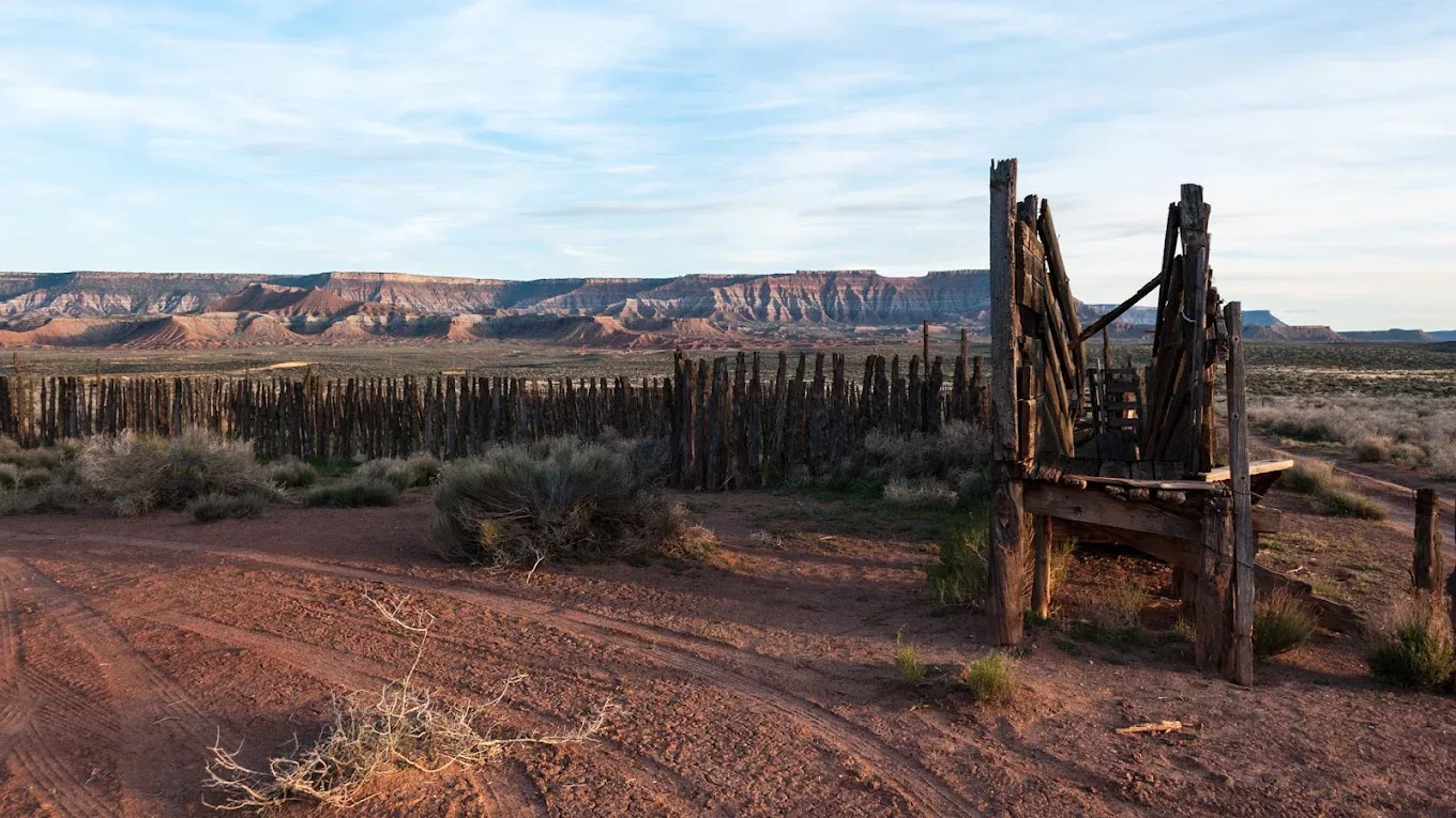An outside view of a desert with an broken and abandoned wagon sits in front of view.