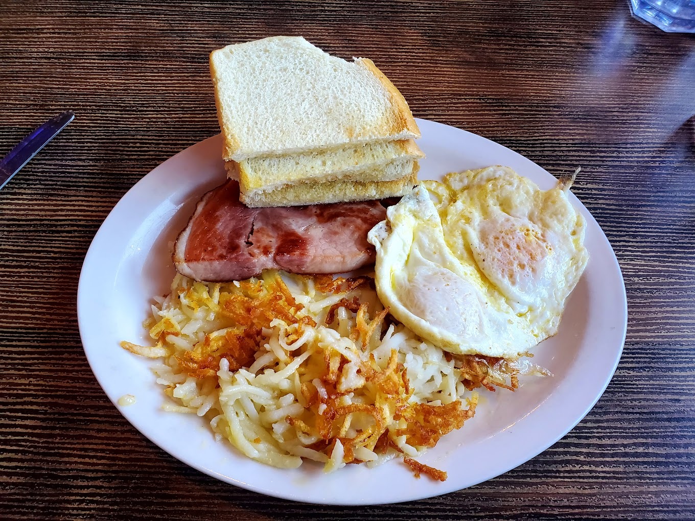 A white plate consisting of hash browns, eggs, and toast.