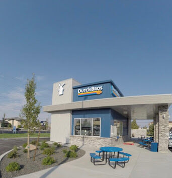 Outside view of the Dutch brothers building. There is a patio with outdoor seating and a drive through area.