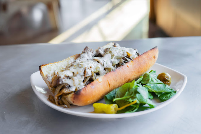 Sandwich meat and sauce in a bun with greens on the side, all on a white plate.