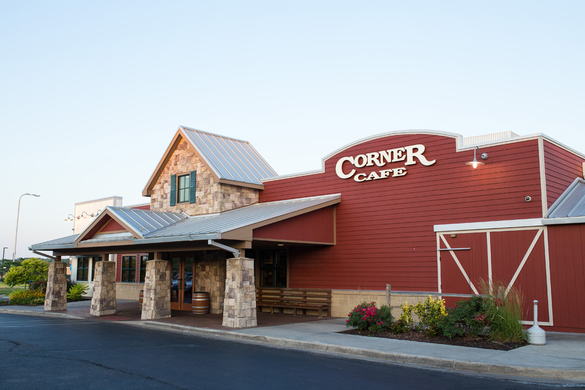 A stone accented building made of red siding, with a large white sign that reads "Corner Cafe"