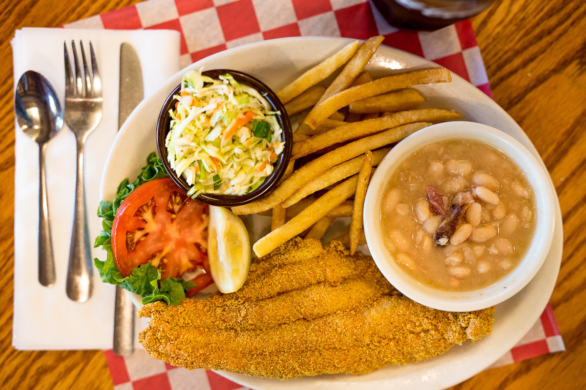 A large white plate with a side of beans, coleslaw, fries, and chicken.
