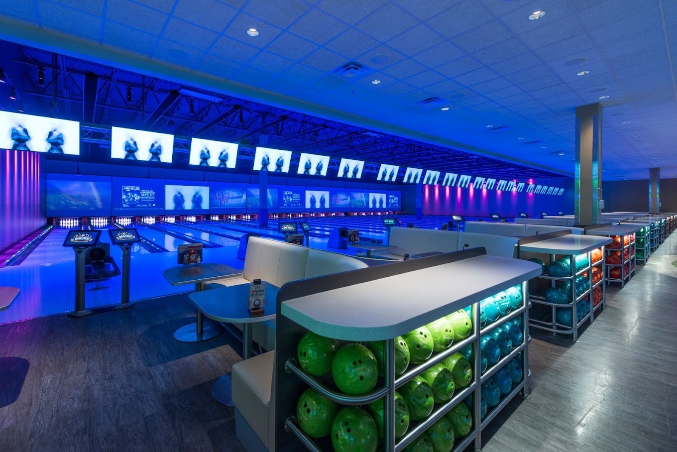 A view of a bowling alley with black lights, TV's lining the wall.