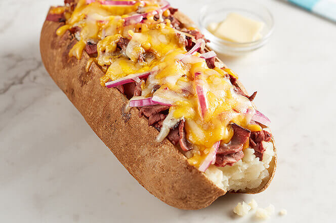A photo of a baked potato on a white background, stuffed with onions, cheese, and meat.