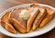 Thick slices of golden-brown French toast dusted with powdered sugar and topped with a scoop of butter on a white plate over a wooden table.