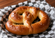 Large golden-brown soft pretzel sprinkled with coarse salt, served on black-and-white checkered paper with a warm wooden background.