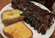 Barbecue pork ribs coated in glossy sauce served with a baked potato and a slice of toasted garlic bread on a white plate in a casual restaurant setting.