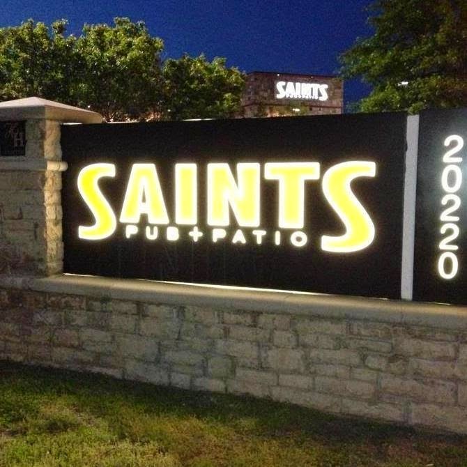 A lighted sign out front of a restaurant. the sign is black and built up on bricks and yellow lighted lettering reading "Saints"