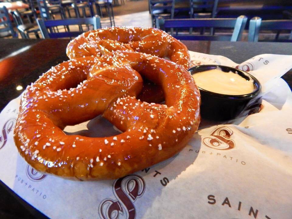 A large soft baked pretzel in a basket with paper and a side of cheese.