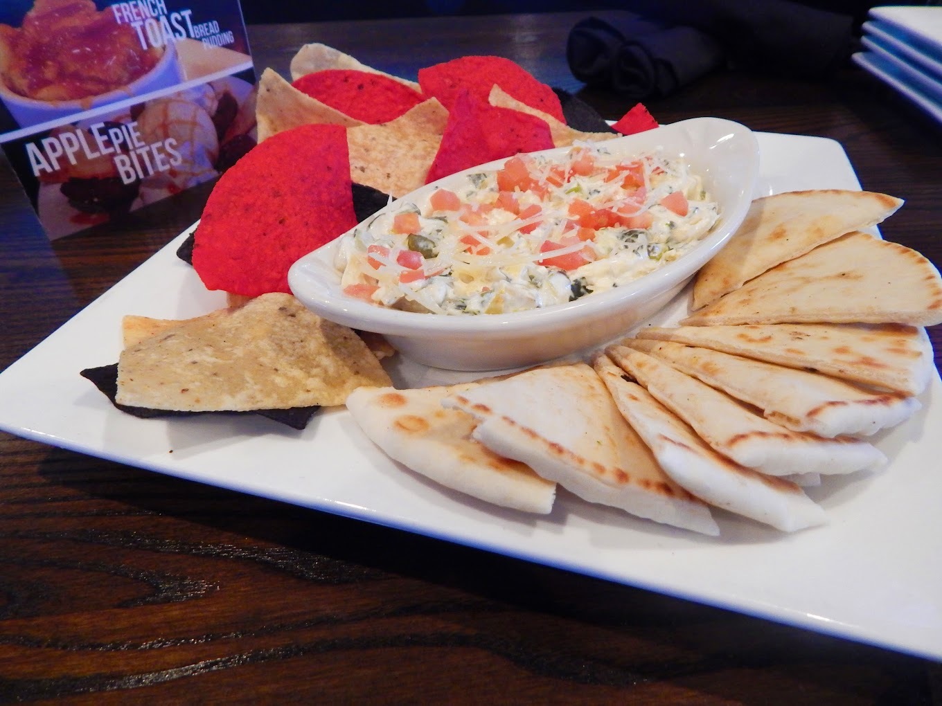 A white plate filled with quesadilla, a side of chips, and loaded queso in a dipping bowl.