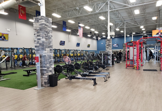 Interior view of two rows of gym equipment. Room features several grey brick columns.