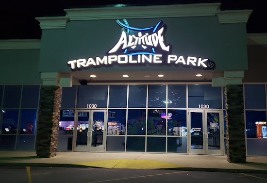 Outside night view of a building with numerous glass windows and doors. Sign above entrance glows and states "Altitude Trampoline Park."