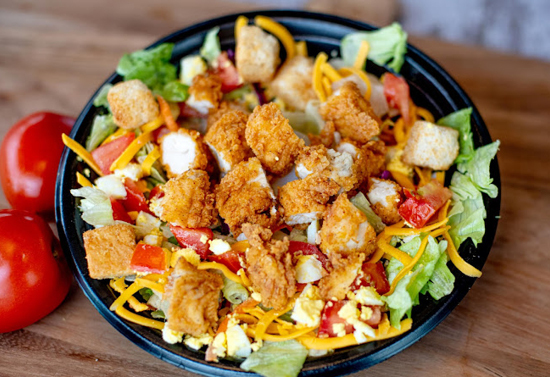 Close view of a green and red salad with breaded chicken.