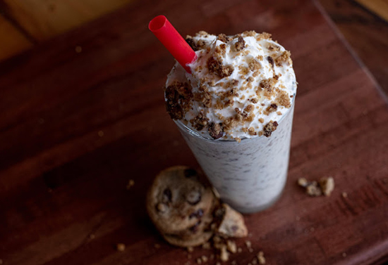 Overhead shot of an iced drink with whipped cream and cookie toppings with a red straw.