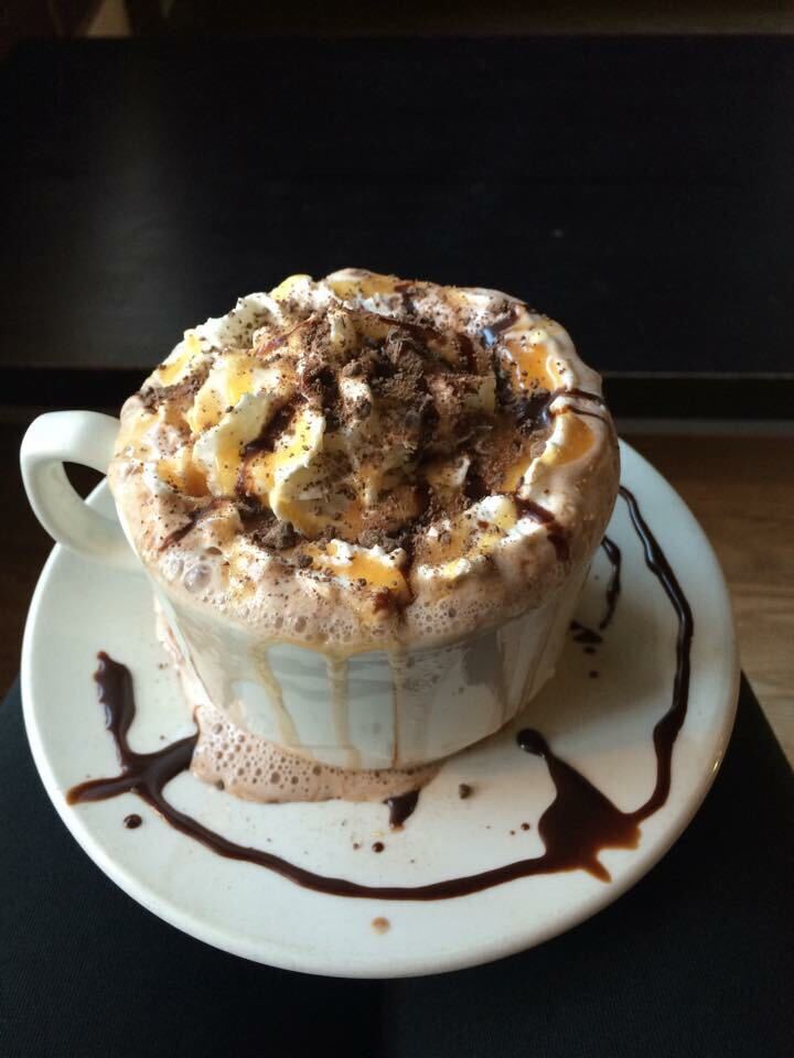A white plate with chocolate drizzle design along with a white cup filled with coffee and topped with whipped cream and topped with butterscotch and chocolate syrup.