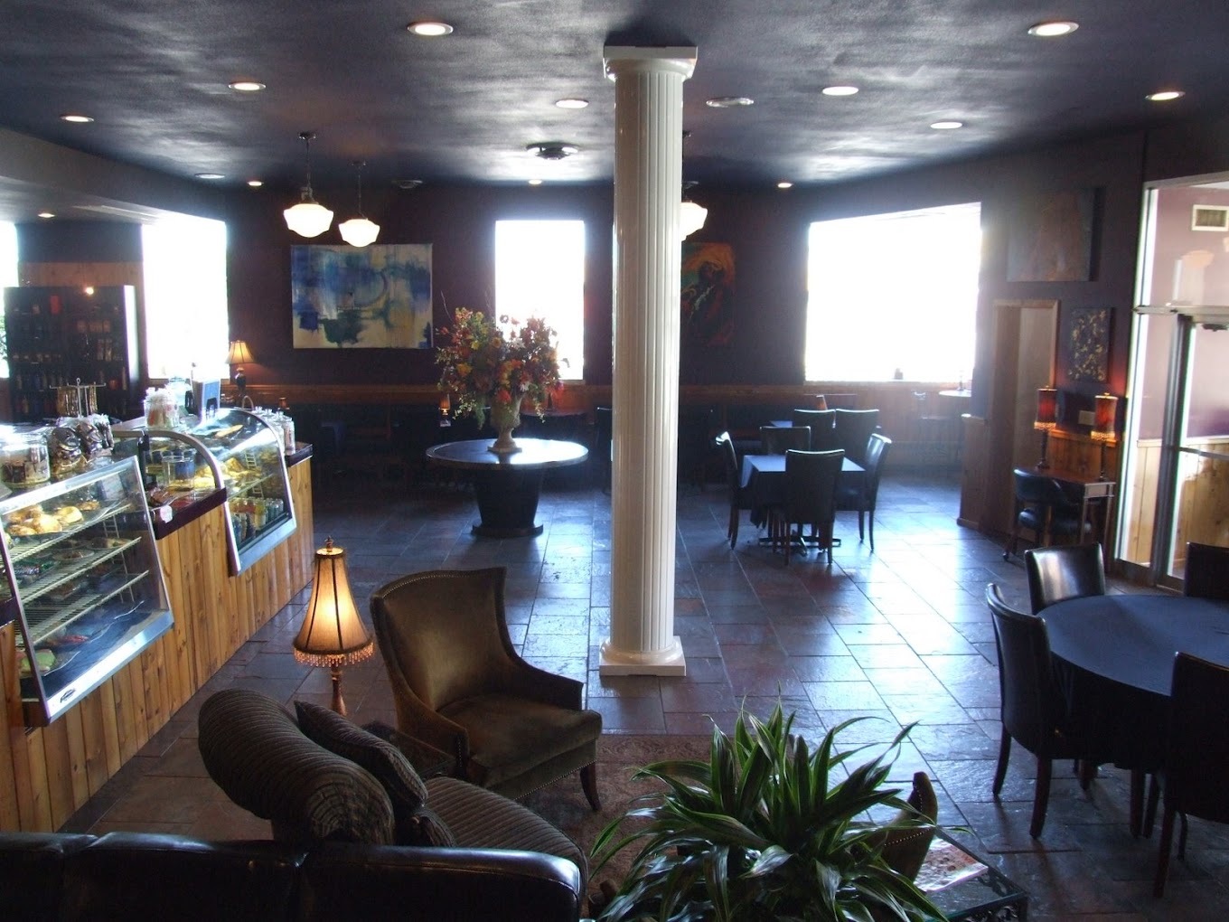 A dimly lit room filled with vintage chairs and tables, along with a counter to the left of the room with a pastry display case.