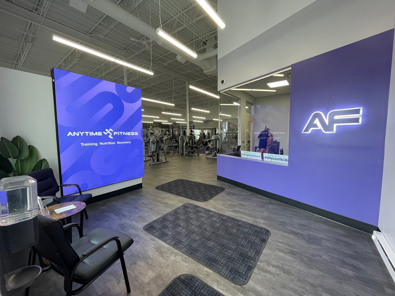 A view of an entrance to a gym, with a large screen on the wall along with a purple wall with an "AF" sign illuminated on the wall.