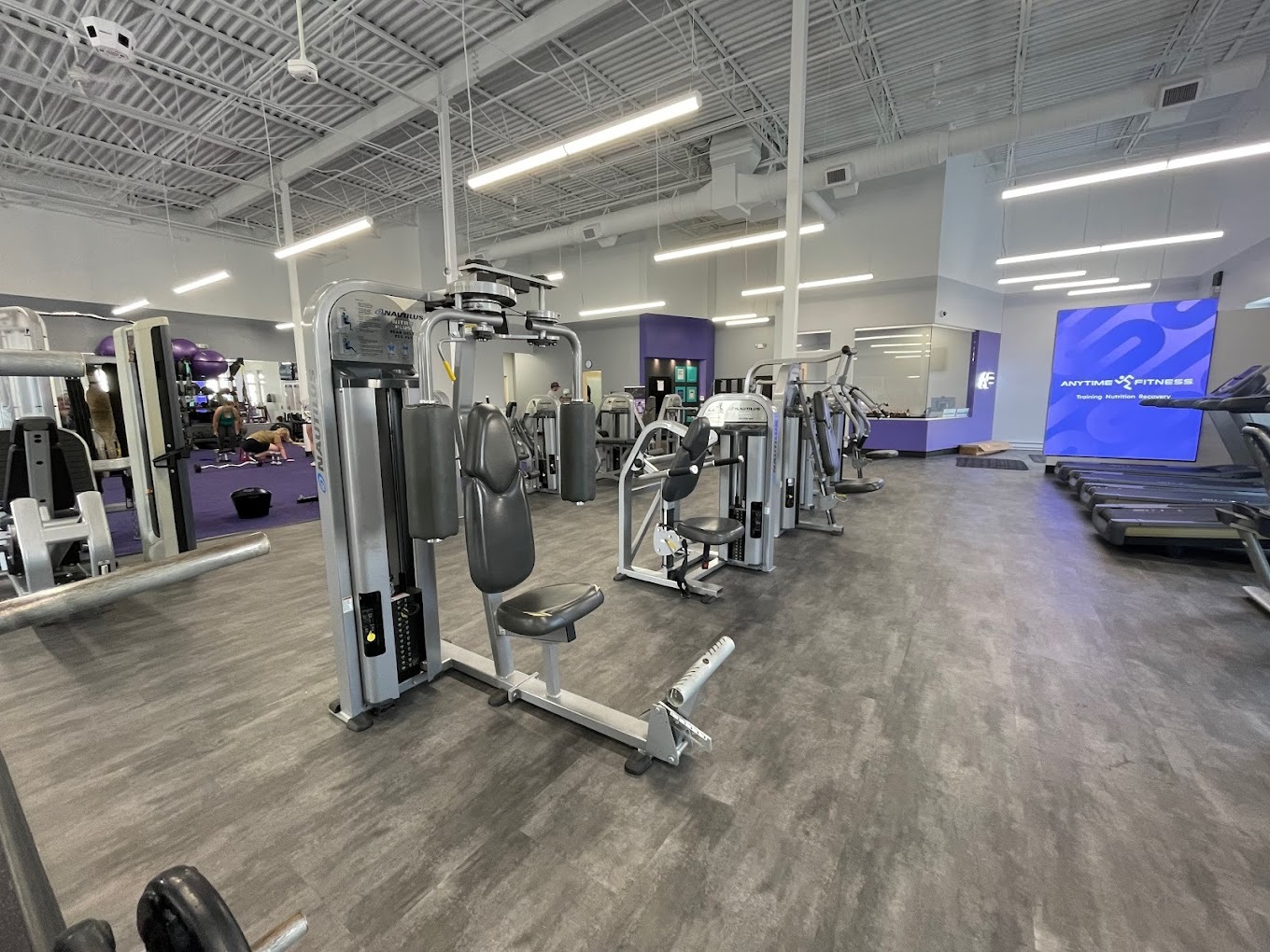 A room with wooden flooring along with lots of work out equipment for strength and cardio.