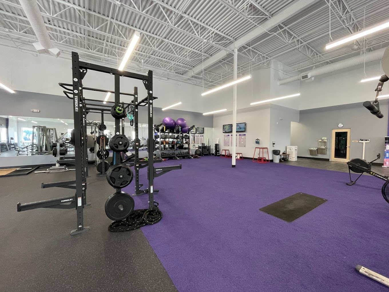 A work out area with a purple floor filled with strength and cardio equipment.