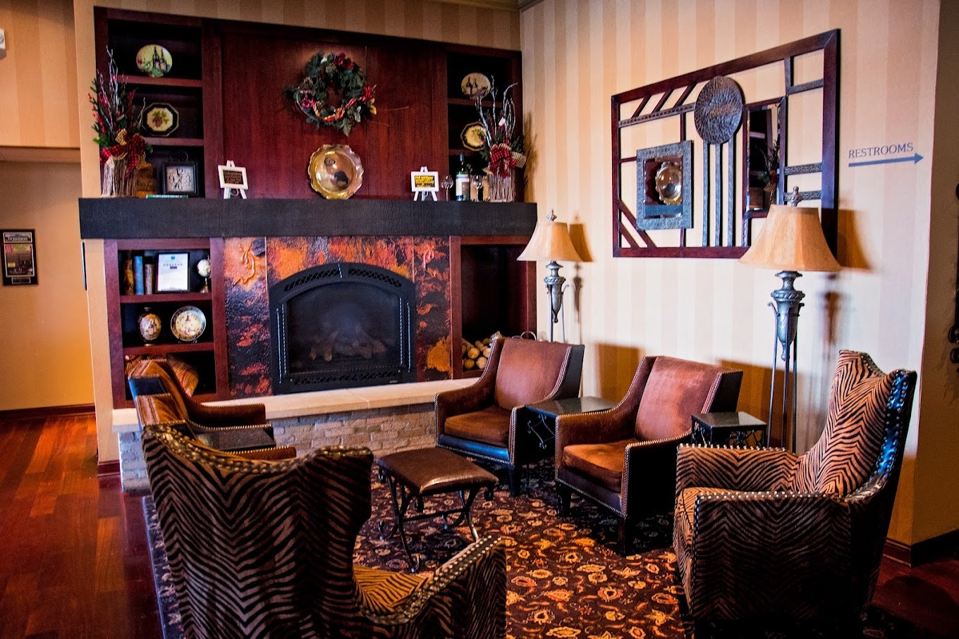 A drawing room filled with chairs surrounding a fireplace along with lots of Knick Knacks setting above the mantle of the fireplace.
