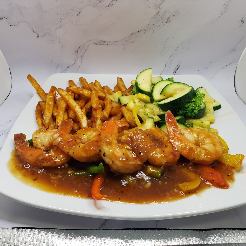 A view of a white plate consisting of shrimp made with a sauce, a side of French fries and a side of veggies.