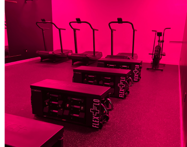 A view of a room lit with infrared lights, a row of treadmills, a running bike, and stepping stairs.