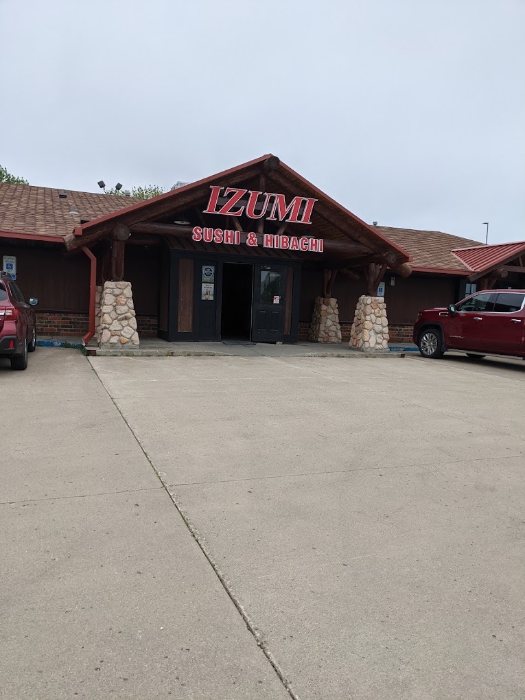 A outside view of a large wooden building with a large red sign above the entrance with the lettering 'Izumi Sushi & Hibachi"