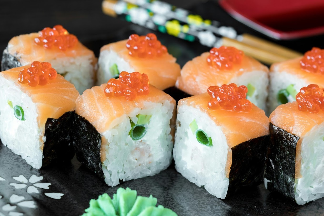 A picture displaying a tray consisting of a sushi roll topped with caviar and chopsticks in a floral wrapping paper.