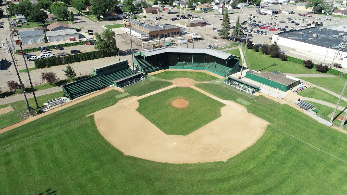 A Birdseye view of a baseball field and baseball stands, a large green field with sand in the middle.