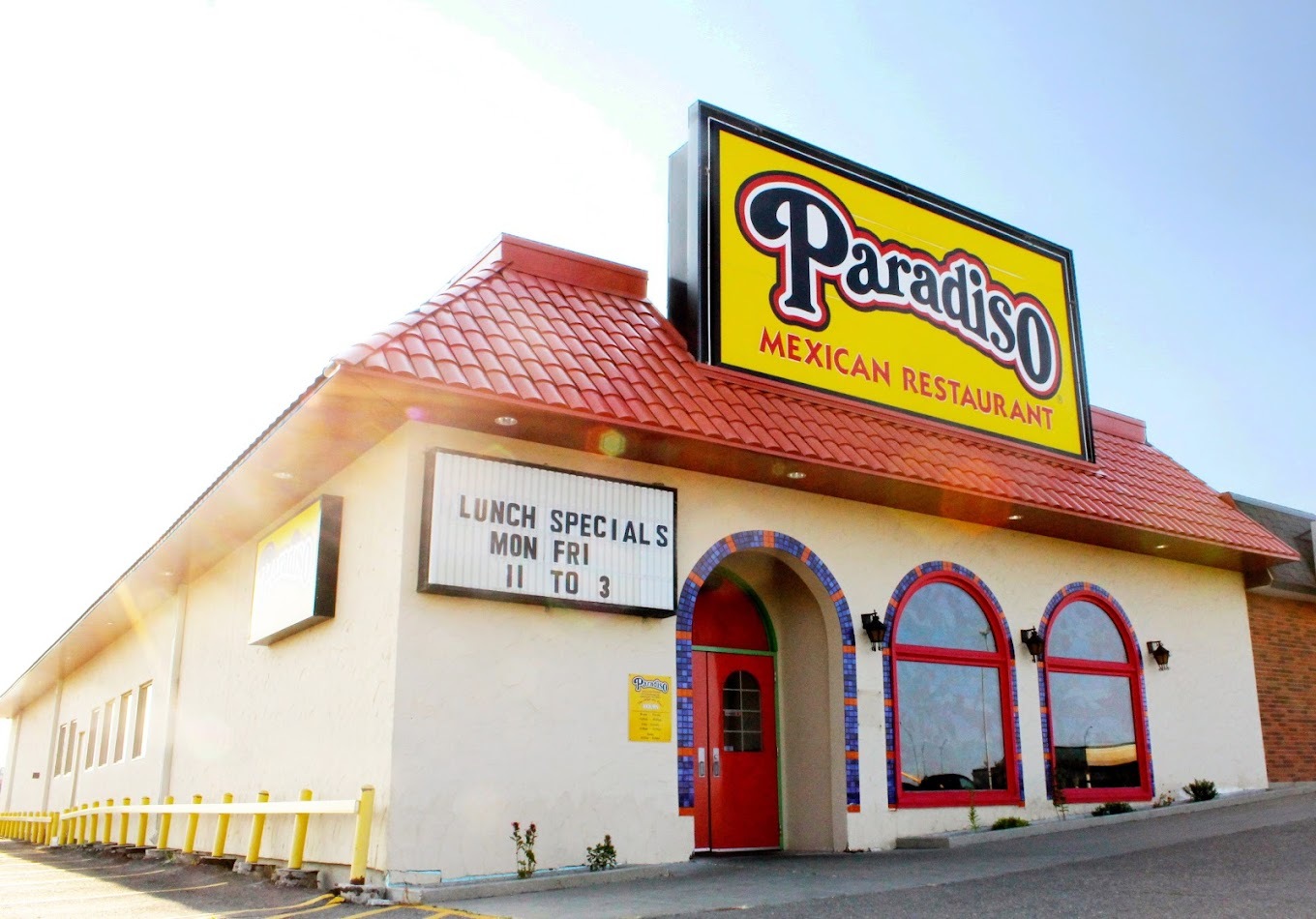 A view of a stucco styled building with a red roof and a very large yellow sign above the bright red door and windows.
