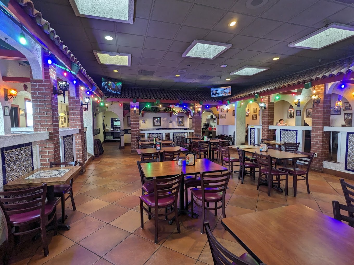 An inside view of a restaurant decorated very festive with colorful string lights filled with tables and chairs along with creative booth seating in the background.