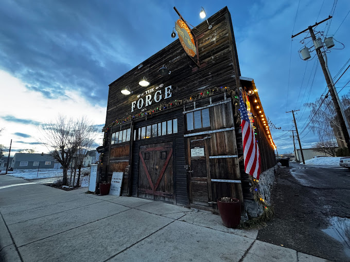 Exterior upward view of a dark wooden building with barn-like doors, Christmas lights, and an American Flag.