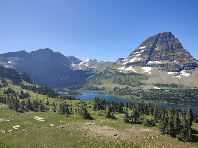 A river flows through the center of the image, with rocky mountains on one side and green trees on the other side.