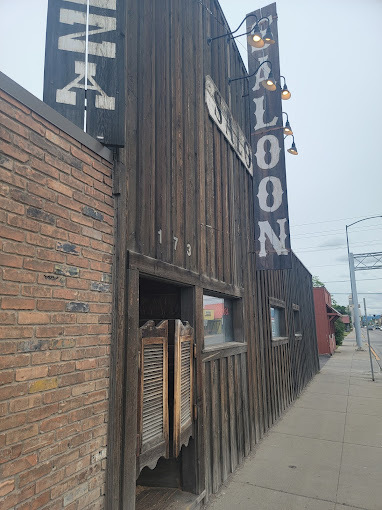 Exterior close view of an old west style building. The entrance is an old saloon type door. The sign on the building is vertical and reads "Saloon."