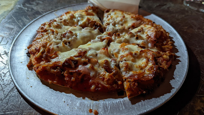 Close view of a cheesy pizza on a metal plate.