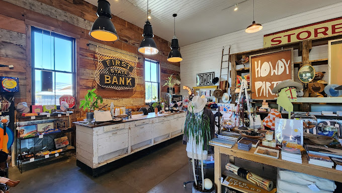 Item filled room with brown wooden wall and a white wooden wall. There is a white wood counter for checkout and a sign behind it that says "First State Bank."