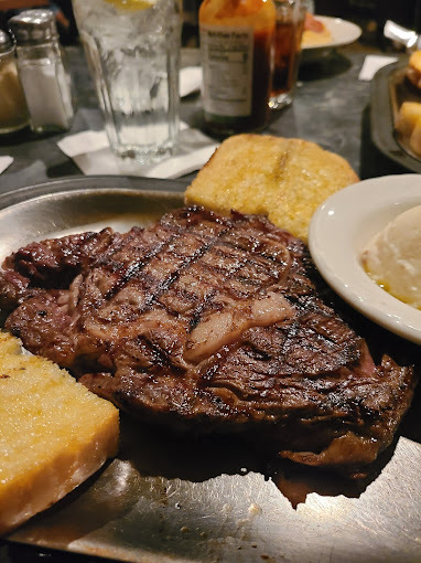 Steak and buttered bread on a stainless steel plate.