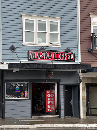 Outside view of a blue slated building with whit framed windows. The center has a canopy and sign that reads "Alaska Coffee."