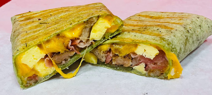 Thin green wrapped sandwich filled with meat and cheese, set on a paper.
