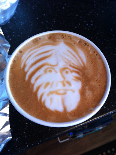 Latte with foamed milk art. Design shows a man with a beard.