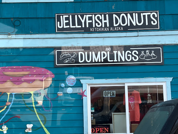 Close outdoor view of a blue slatted building. Illustration next to the door is a doughnut jellyfish. Two signs are above the door stating the business name.
