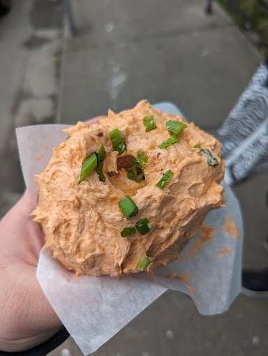 Hand holding a seafood based doughnut in a white paper.