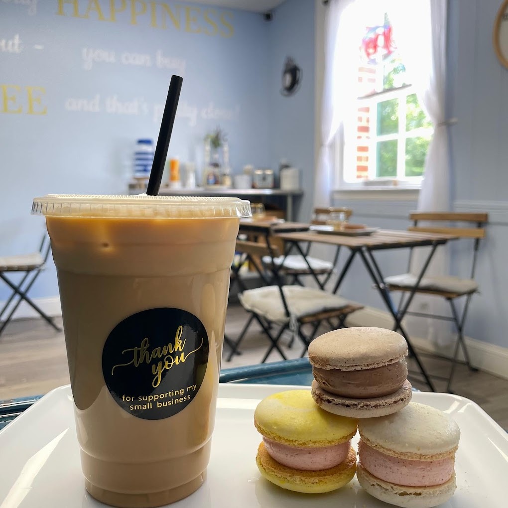 A white serving tray with an iced coffee and a stack of three French macaroon cookies.