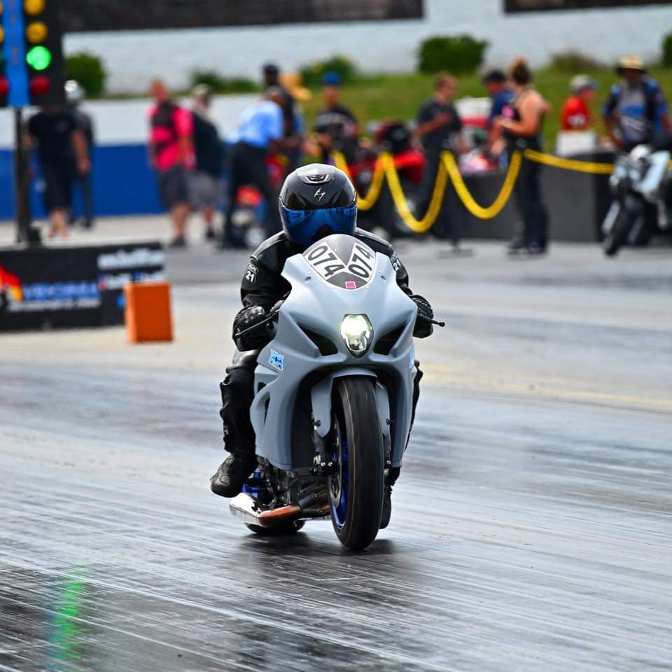 A motorcyclist riding his bike on the drag strip, wearing a helmet driving an grey motorsports bike.