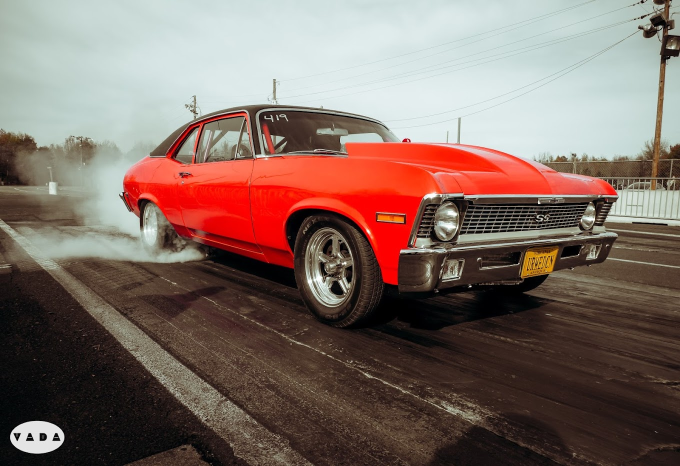 A view of a car rolling smoke from its back tires on the drag strip, a red vintage muscle car.